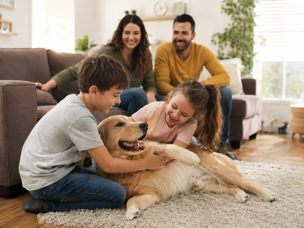Two children playing with a golden retriever on a living-room rug while their parents watch from the sofa